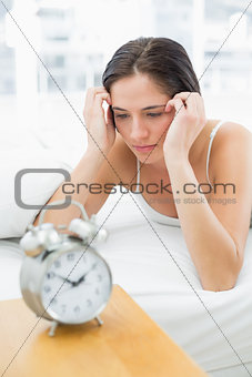 Woman looking at alarm clock while lying in bed