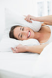 Smiling woman covering ears with pillow in bed