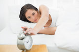 Woman extending hand to alarm clock at home