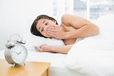 Shocked woman in bed looking at alarm clock