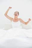 Cheerful woman yawning while stretching arms in bed