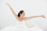 Smiling young woman stretching arms in bed