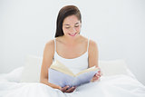 Smiling woman reading a book in bed
