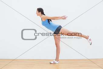 Full length of a woman standing on one leg in fitness center