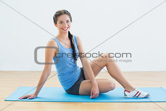 Full length of a smiling woman sitting on exercise mat