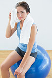 Woman with towel around neck sitting on exercise ball