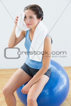 Tired woman with towel around neck on exercise ball