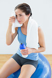 Tired woman with towel around neck and waterbottle on exercise ball