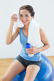 Woman with towel around neck and waterbottle sitting on exercise ball