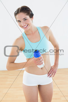 Fit smiling woman holding water bottle at fitness studio