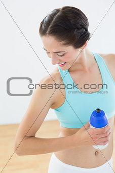 Fit smiling woman holding water bottle at fitness studio
