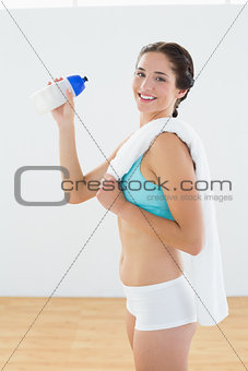 Fit smiling woman with water bottle and towel at fitness studio