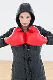 Serious woman in red boxing gloves and black hood at fitness studio