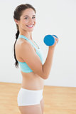 Smiling young woman with dumbbell at fitness studio