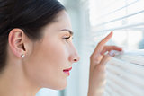 Young business woman peeking through blinds at office
