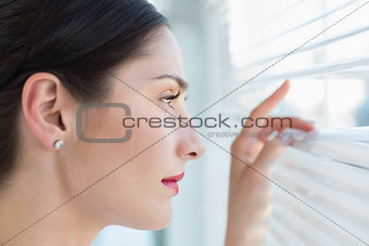 Young business woman peeking through blinds at office