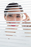 Smiling young business woman peeking through blinds