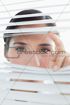 Young business woman peeking through blinds