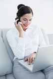 Well dressed woman using laptop and cellphone on sofa