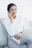 Well dressed woman using laptop and cellphone on sofa