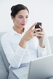 Well dressed woman using cellphone and laptop on sofa