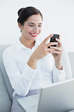 Smiling well dressed woman using cellphone and laptop