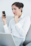 Well dressed woman using cellphone and laptop on sofa