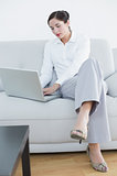 Full length of a well dressed woman using laptop on sofa