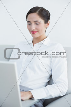 Smiling well dressed woman using laptop on sofa