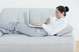 Side view of a well dressed woman with laptop and coffee cup on sofa