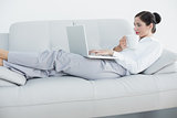 Well dressed woman with laptop and coffee cup on sofa