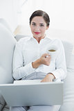 Well dressed woman with laptop and coffee cup on sofa
