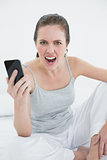 Portrait of an angry woman shouting with mobile phone in hand