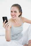 Smiling woman with mobile phone sitting in bed