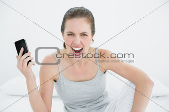 Angry woman shouting with mobile phone in hand on bed