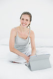 Smiling casual woman using tablet PC in bed