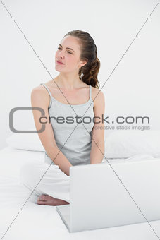 Casual woman with laptop looking to her side in bed