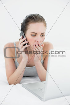 Shocked casual woman using cellphone and laptop