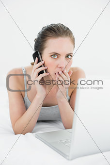 Portrait of a shocked casual woman using cellphone and laptop