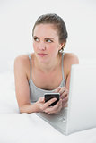 Woman with cellphone and laptop lying in bed