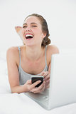 Cheerful casual woman using cellphone and laptop