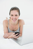 Casual woman with cellphone and laptop in bed