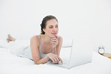 Thoughtful casual woman using laptop in bed
