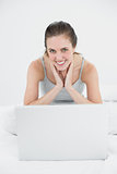 Portrait of a smiling casual woman with laptop sitting in bed