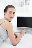 Thoughtful casual woman with laptop in bed