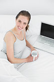 Casual woman with laptop and tea cup in bed