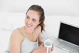 Thoughtful casual woman with laptop and coffee cup in bed