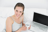 Portrait of a smiling casual woman with laptop and coffee cup in bed