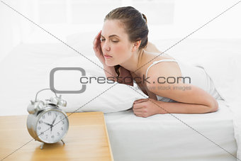 Sleepy woman in bed with alarm clock in foreground