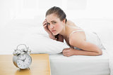 Displeased woman in bed with alarm clock in foreground